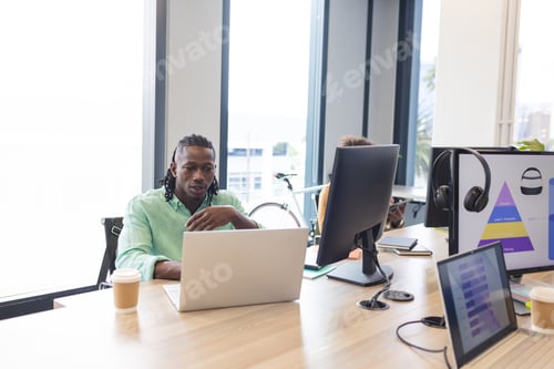 Preview: African American man with braided hair working on a laptop in a modern business office