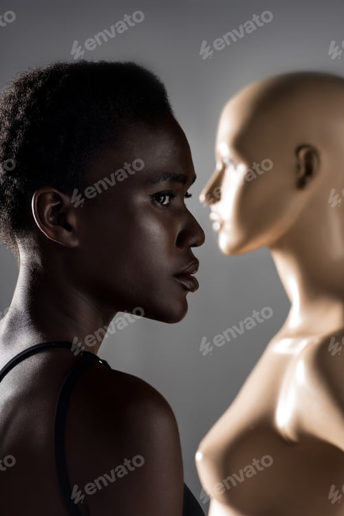 Preview: profile portrait of beautiful african american girl looking away while standing near mannequin on