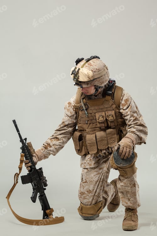 Preview: Soldier kneeling with weapon and gear during training indoors in neutral background