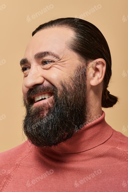 Preview: positive man with beard in pink turtleneck jumper smiling cheerfully on beige backdrop