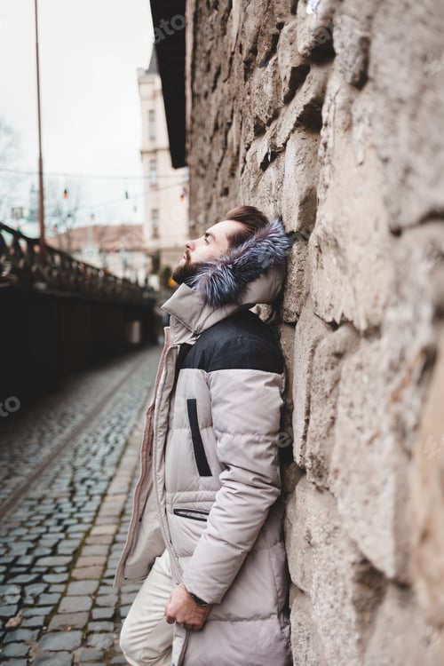 Preview: Stylish handsome man with a beard in a winter jacket with fur posing outdoors.