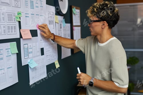 Preview: Young Adult Caucasian Man Planning Mobile App Interface Design on Wall