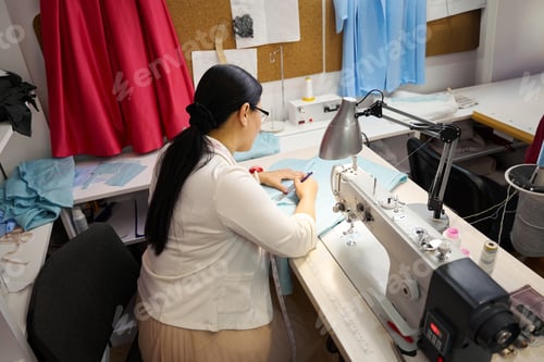 Preview: Dressmaker at workplace works with blue fabric