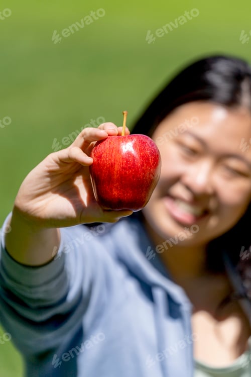 Vista previa: Mujer asiática que muestra una manzana roja en el parque