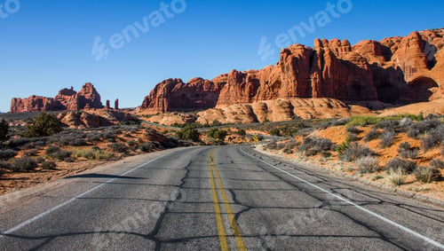 Preview: Beautiful shot of an empty road in the middle of a desert with bushes and cliffs in the distance
