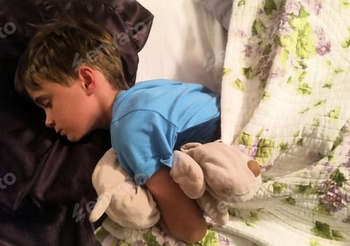 Preview: Bed vibes as generation z boy sleeping in bed with his stuffed animal for comfort and security.