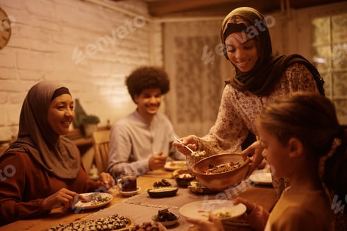 Preview: Happy Middle Eastern woman serving food during family dinner at dining table.
