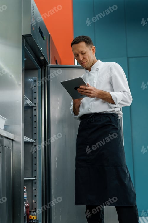 Preview: Professional chef using tablet computer for recipes while working in modern kitchen cooking concept