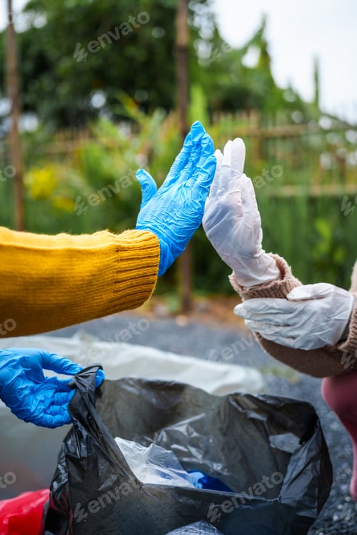 Preview: Close-up of young women girls hands sorting recyclable plastic bottles into trash bags outdoors