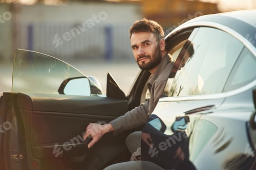 Preview: Sitting on the seat. Man is standing near his electric car outdoors
