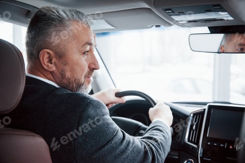 Preview: View from behind of senior businessman in official clothes driving a modern new car