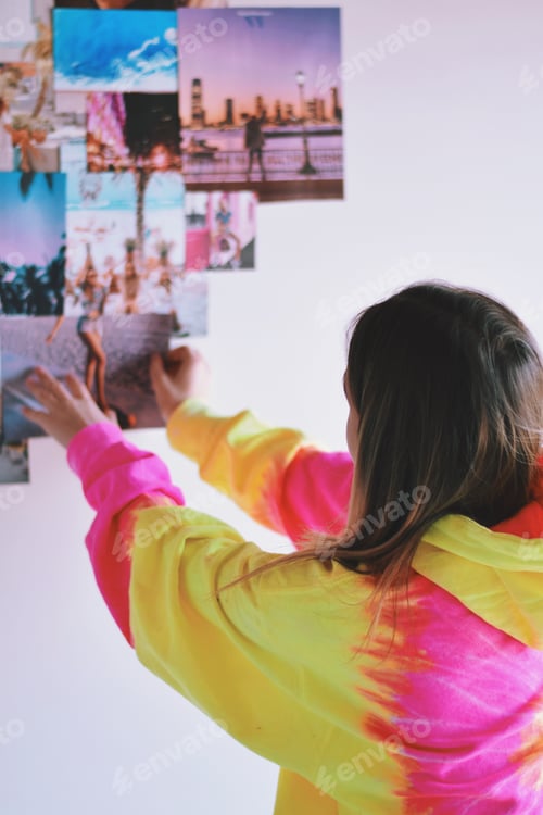 Preview: Young teenage girl is sticking inspirational magazine cutouts on a wall in her bedroom