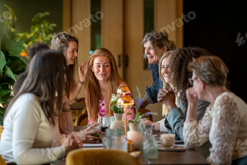Preview: A group of joyful women engaging in conversation around a dining table in a warm, well-lit room.