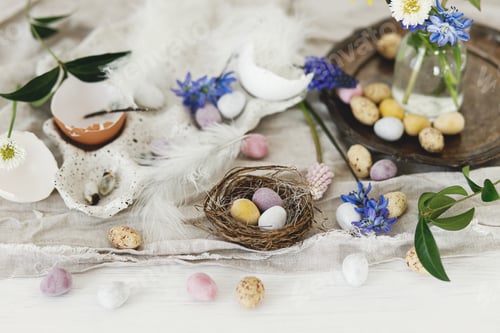 Preview: Colorful easter chocolate eggs in nest, spring flowers, chicken figurine and linen cloth