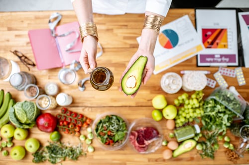 Preview: Dietitian holding avocado and olive oil above the table full of healthy food