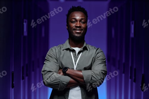 Preview: Black young man standing in server room with arms crossed and looking at camera