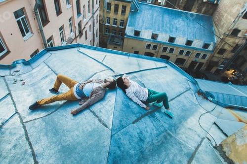 Preview: Young hipster couple lying on the roof and kissing. Beautiful view of the city from above. Casual