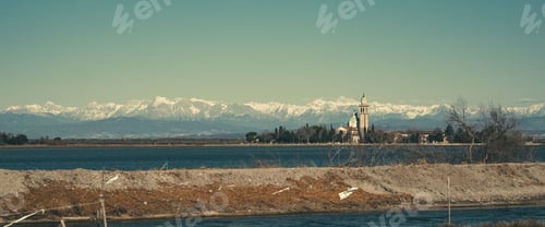 Preview: Scenic view of a historic church by the water with snow-capped mountains in the background