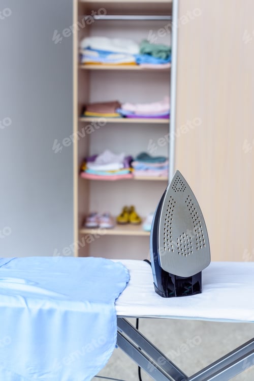 Vista previa: close-up shot of iron on board in front of cabinet with clothes