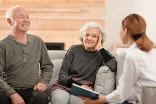 Preview: Female caregiver reading book to elderly spouses in living room