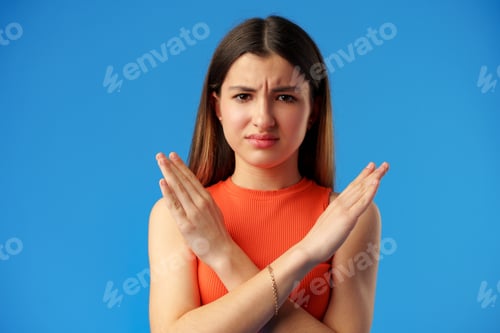 Preview: Teen girl shows cross hands gesture, rejecting something over blue background in studio