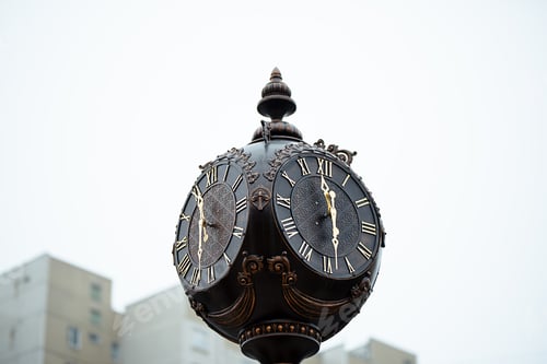 Preview: Horizontal photo of a street metal brown round clock with Roman numerals close-up.