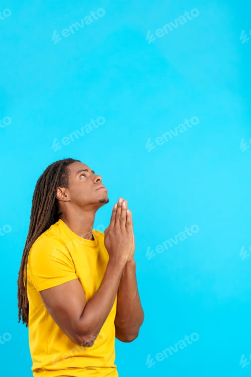 Preview: Latin man with dreadlocks looking up praying with folded hands