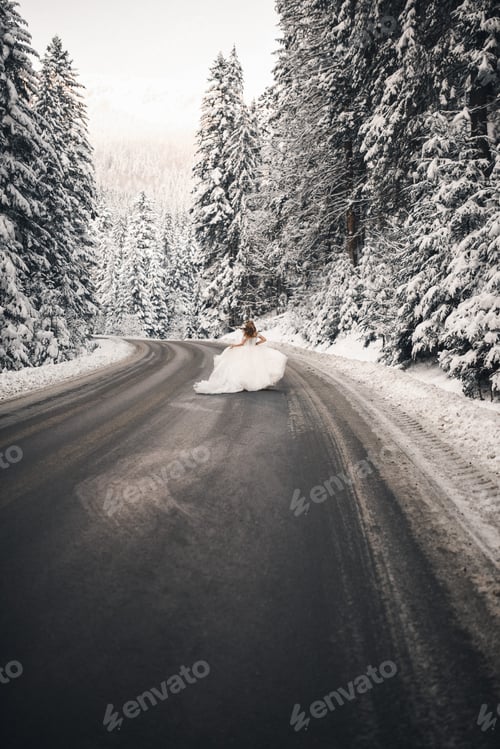 Preview: bride runs along the road near the snowy tall fir trees