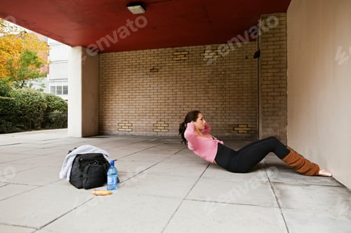 Preview: A person is seen exercising, doing sit-ups on the ground under a covered outdoor area