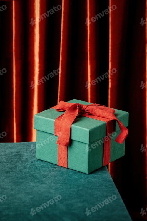 Preview: Green gfit box with red bow on fabric surface and curtains on background