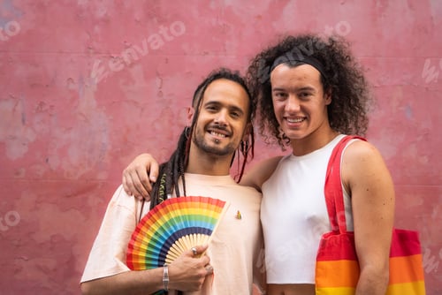 Preview: Two men are posing for a picture, one of them holding a rainbow fan