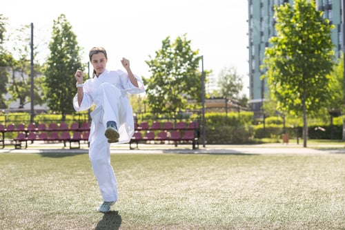 Preview: Young active girl wearing in white kimono with white belt performing martial arts kick skills