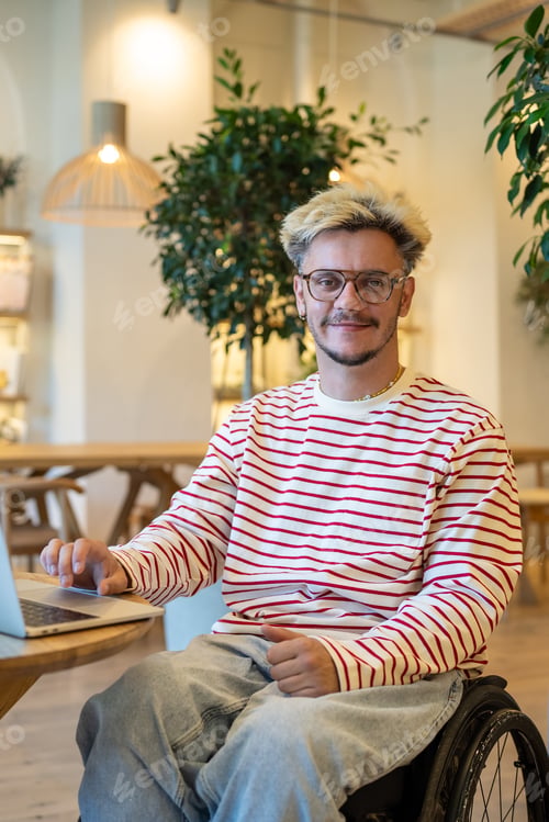 Preview: Portrait disabled man freelancer on wheelchair sits on adaptive place in coffee shop with laptop.