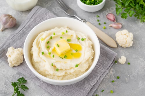 Preview: Cauliflower puree with butter and green onions in a white bowl. Healthy food. Copy space.