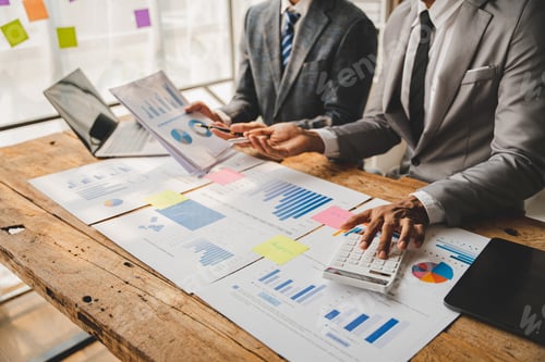 Preview: Young colleagues discuss business and analytical price charts using calculators and laptops to calcu