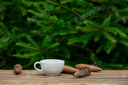 Preview: cup of coffee and pine cones on wooden table with spruce branches on background