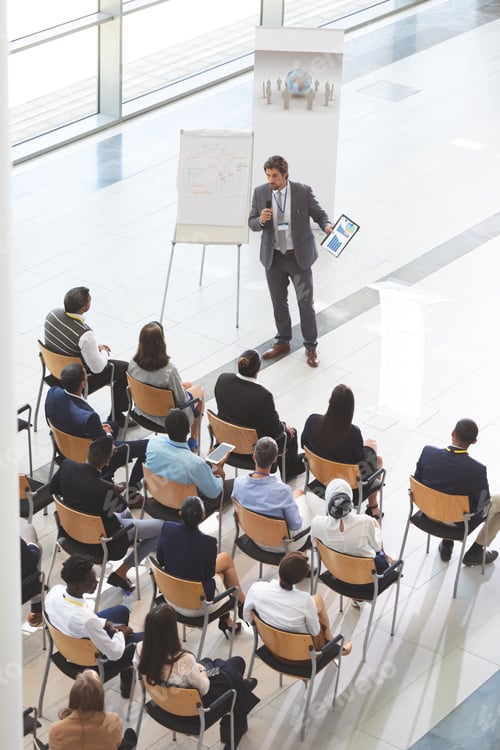 Preview: Businessman speaking while holding digital tablet and microphone at conference.