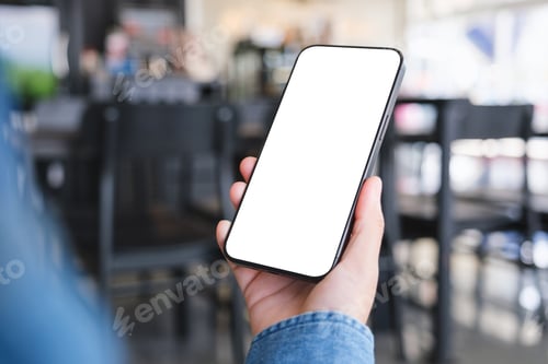 Preview: Mockup image of a woman holding and using mobile phone with blank desktop in cafe
