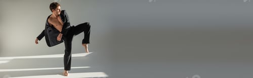 Preview: full length of trendy barefoot man in black pants and blazer on shirtless body posing on one leg on