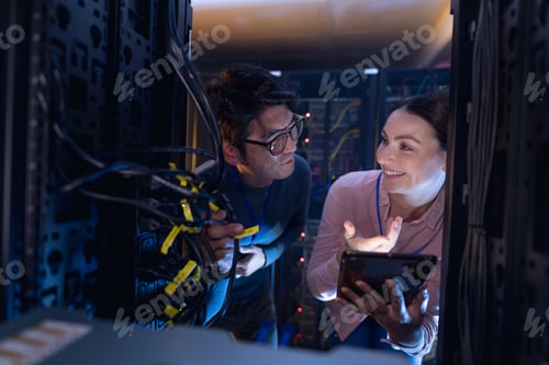 Preview: Diverse male and female engineers with digital tablet inspecting the server in computer server room
