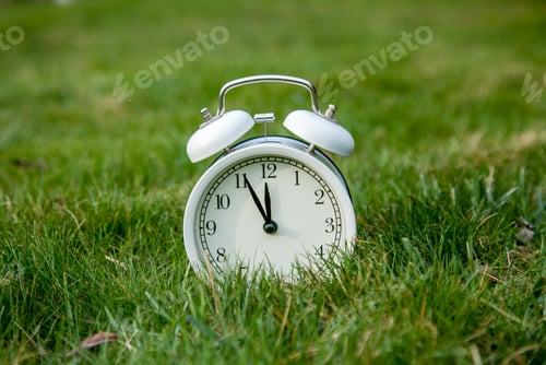 Preview: White classic alarm clock with bells on green grass in a spring