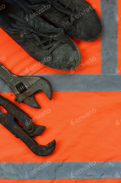Preview: Adjustable wrenches and old boots lies on an orange signal worker shirt