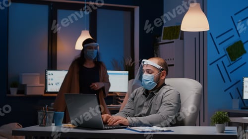 Preview: Workaholic businessman with face mask and visor against covid19 working in company office