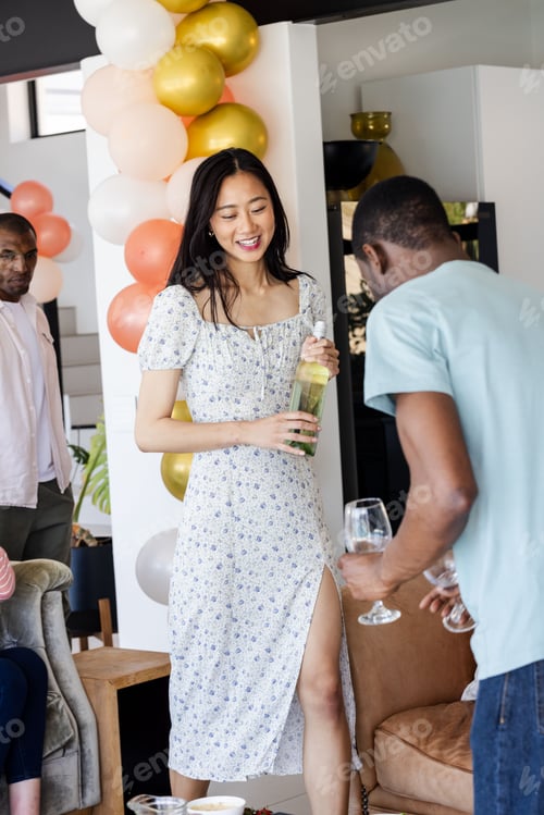 Preview: Friends celebrating at home, woman holding bottle while others enjoy drinks