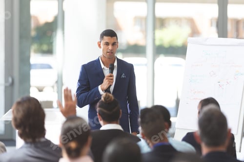 Preview: Businessman speaking in front of diverse group of people with microphone at conference