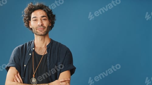 Preview: Man with curly hair, dressed in blue shirt, looks at camera, isolated on blue background in studio