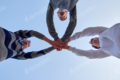 Preview: Low angle shot of three young friends putting their hands together against a blue sky