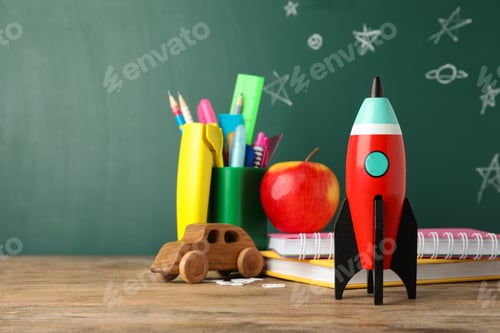Preview: Bright toy rocket and school supplies on wooden desk. Space for text