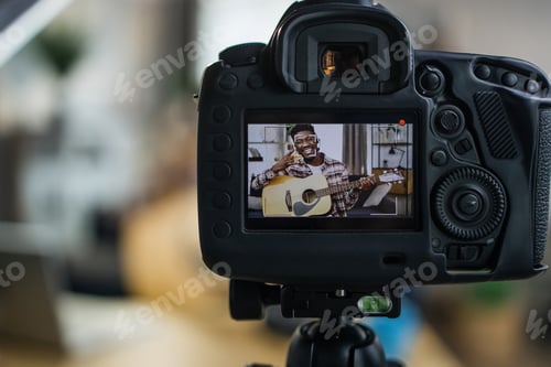 Preview: Cheerful man recording video on camera while playing guitar