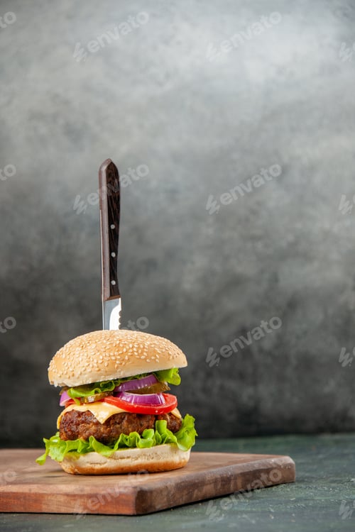 Preview: Knife in delicious meat sandwich on wooden cutting board on isolated dark background